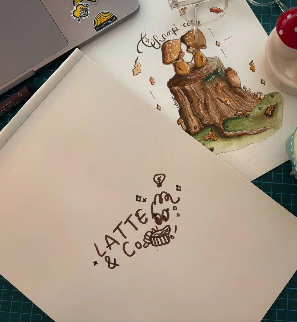 Logo de l'agence Latte&amp;Co dessiné sur une feuille aux côtés d'illustrations sur un espace de travail.